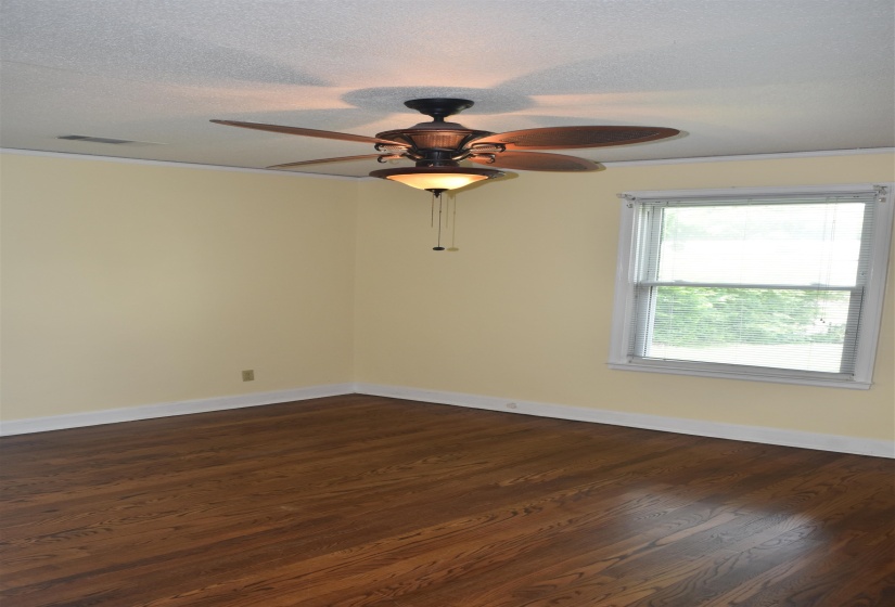 Spacious room with wood-finish flooring, a ceiling fan with integrated lighting, a double-hung window, white baseboards, and crown molding