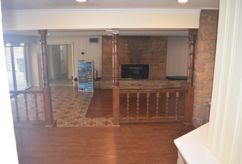 Living area featuring wood-finish flooring, a stone accent wall with a built-in fireplace, and a partial wood railing