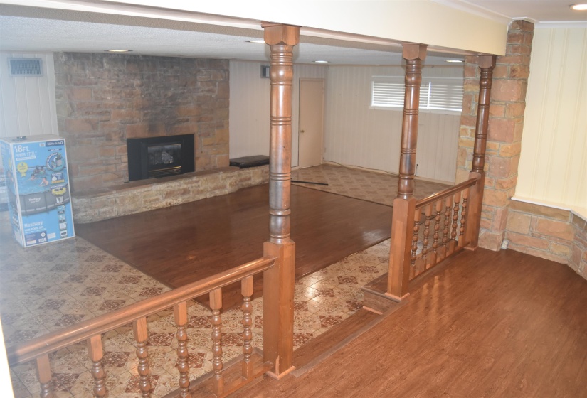 Lower-level living area featuring a stone-clad fireplace and hearth, wood-finish flooring, and a stone-accented wall
