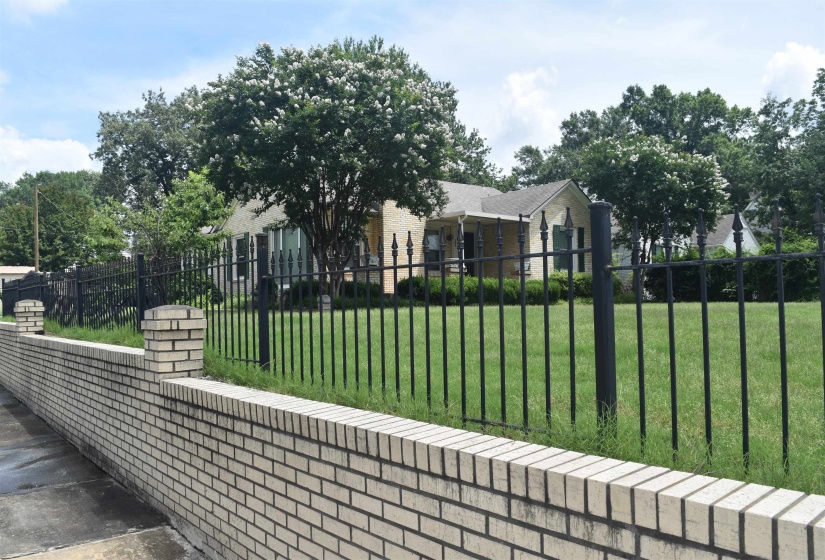 Front yard featuring a light-colored brick retaining wall with decorative posts, a black wrought iron fence, and a manicured lawn