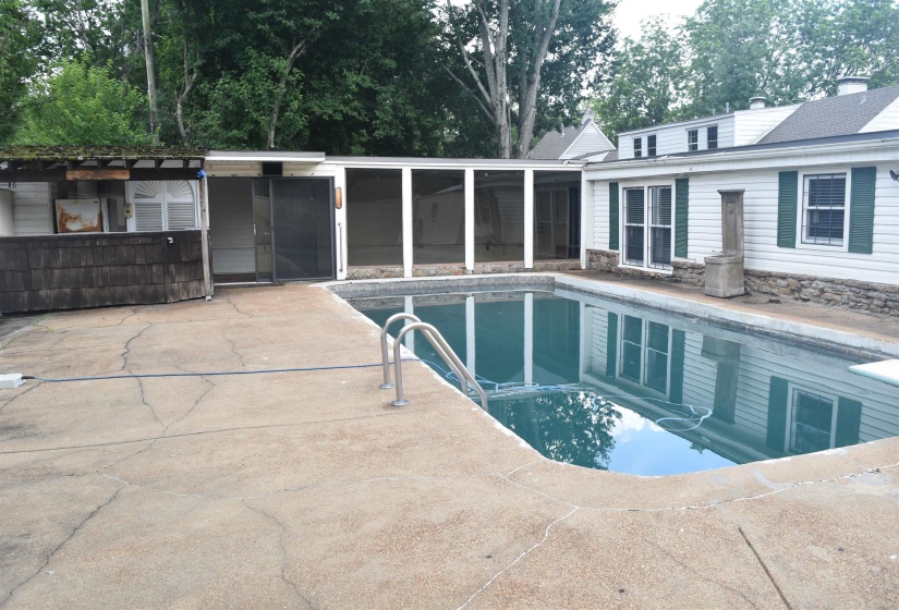 Rectangular swimming pool featuring a concrete surround, metal access rails, and an adjacent screened-in patio area