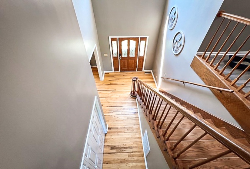 Foyer featuring a grand entrance with a solid wood door and sidelights, hardwood flooring, a vaulted ceiling, and a prominent staircase with wood balusters and handrails