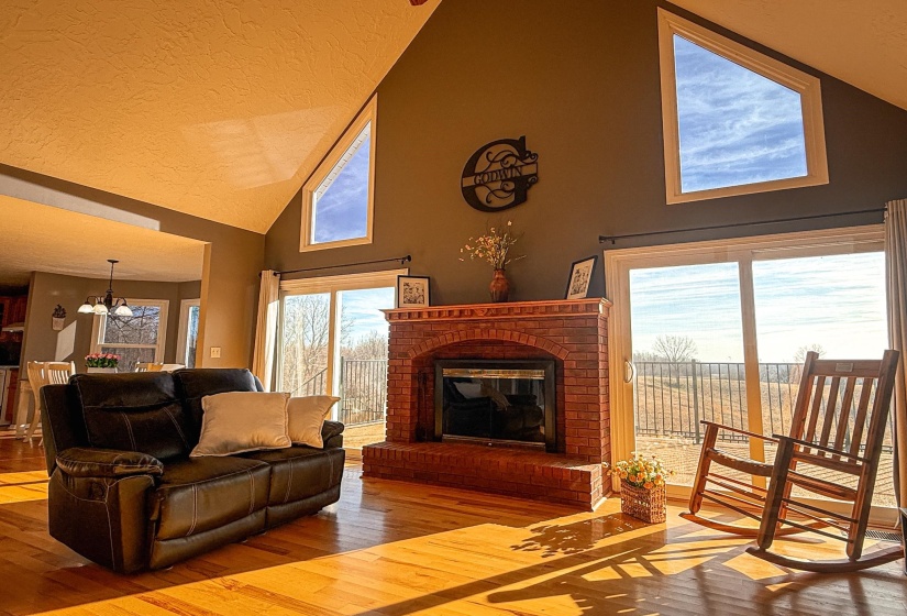 Living area featuring vaulted ceilings, wood-finish flooring, a brick fireplace, and sliding glass doors leading to an outdoor space