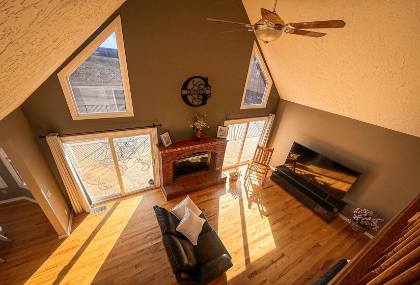 Vaulted ceiling with a ceiling fan, hardwood flooring, and a brick fireplace
