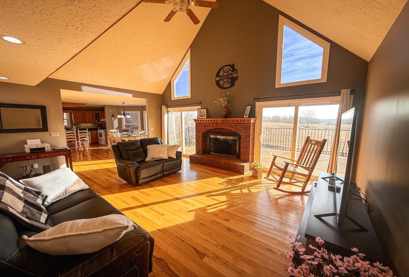 Vaulted ceiling living area featuring wood-finish flooring, a brick fireplace, and direct access to an exterior deck through sliding glass doors