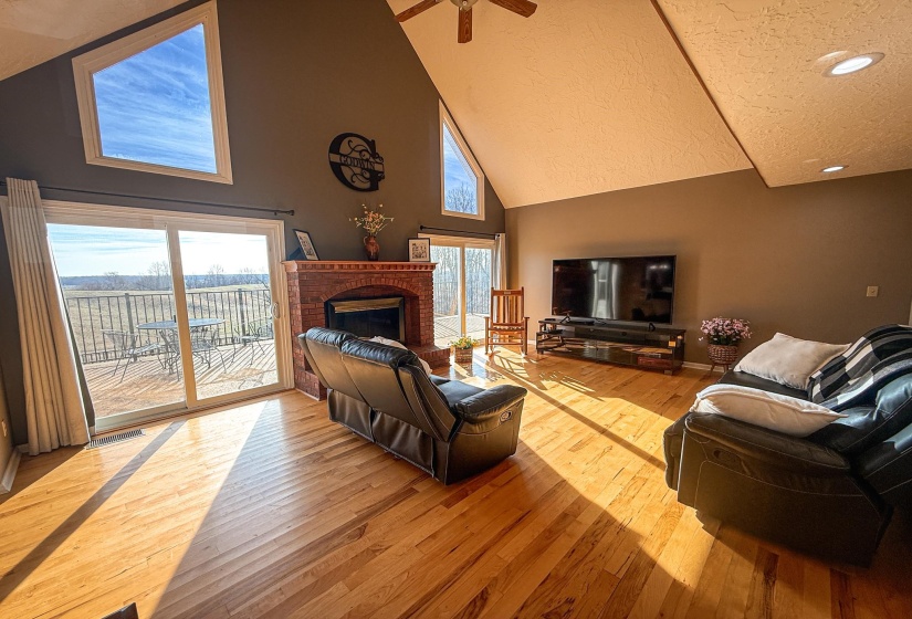 Vaulted ceiling great room featuring wood-finish flooring, a brick fireplace, and dual sliding glass doors opening to a deck