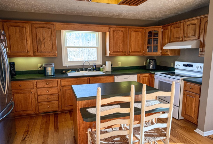 Kitchen featuring wood-finish cabinetry, a central island with countertop seating, a double basin sink, and wood-finish flooring