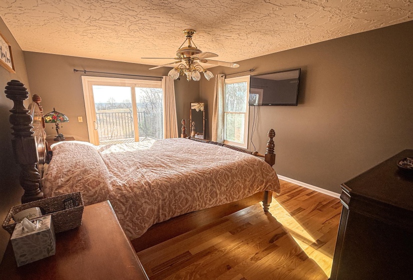 Bedroom featuring sliding glass doors to an exterior balcony, wood-finish flooring, a ceiling fan with integrated lighting, and neutral tone walls