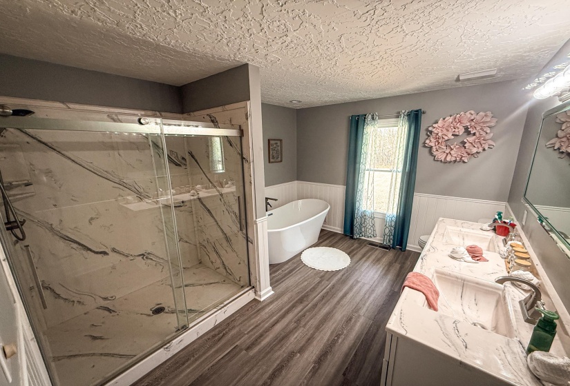 Spacious bathroom featuring a frameless glass shower enclosure with marble-look surrounds, a freestanding soaking tub, and dual vanity with integrated marble-look sinks