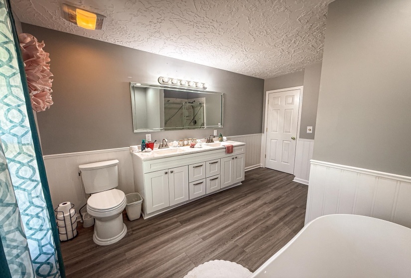 Well-appointed bathroom featuring wood-finish flooring, wainscoting, and a double vanity with ample counter space