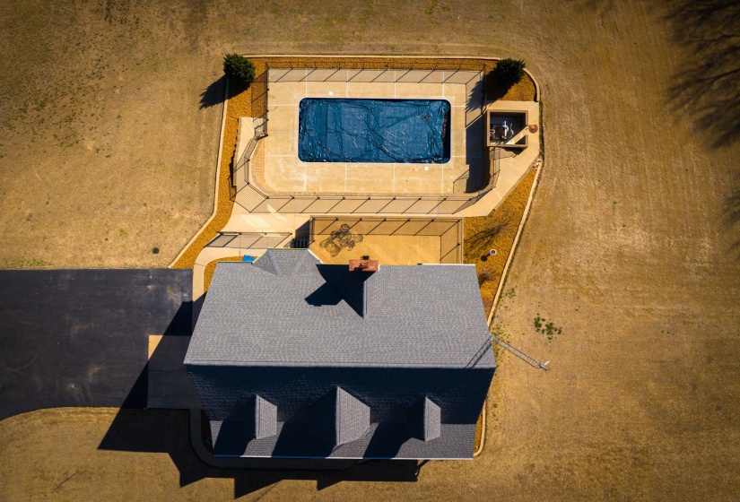 Aerial view showcasing a rectangular in-ground swimming pool with a covered surface, surrounded by a paved patio and fencing