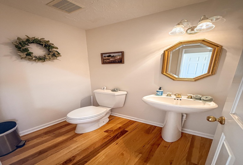 Hardwood flooring complements a white pedestal sink with brass-toned fixtures