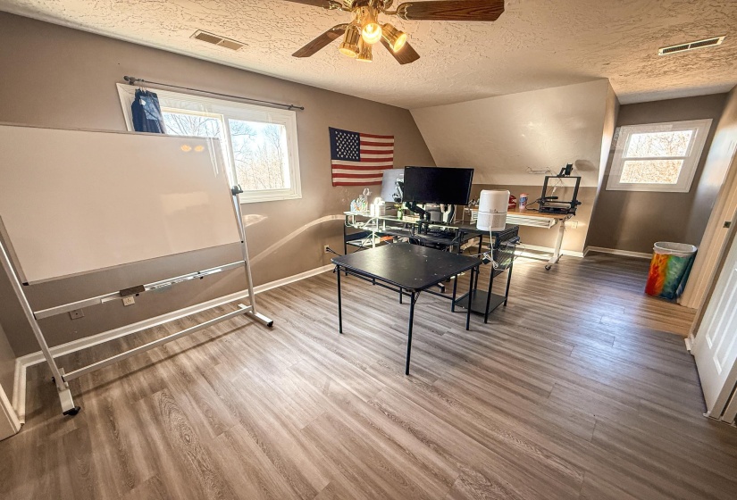 Room featuring wood-finish flooring, a ceiling fan with integrated lighting, multiple windows, and angled wall sections