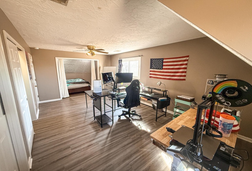 Spacious room featuring wood-finish flooring, a ceiling fan, and multiple windows providing natural light