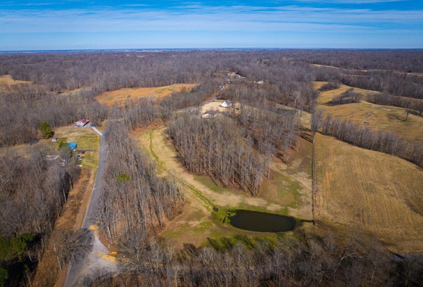 Expansive aerial showcasing a large tract of land featuring mature trees, open fields, and a private pond