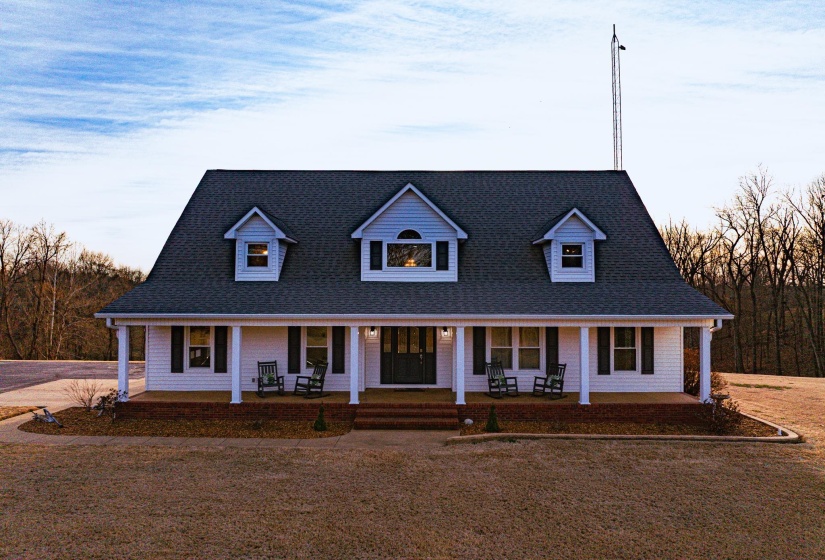 White-sided residence featuring a covered front porch with white columns, a dark shingle roof, and multiple dormer windows