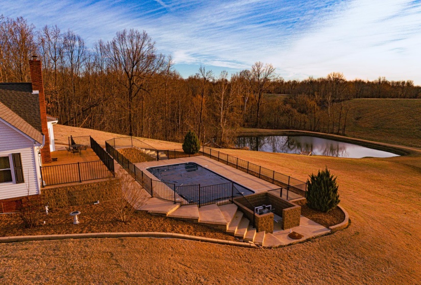 Expansive property featuring a covered pool with surrounding concrete patio, a multi-level deck, a built-in outdoor grilling station, mature trees, and a private pond