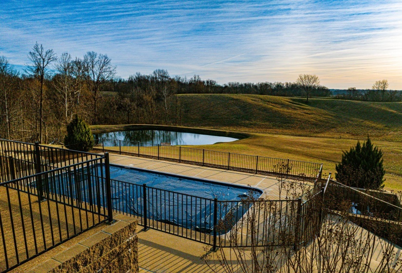 Outdoor swimming pool with a black safety fence, surrounded by a concrete patio