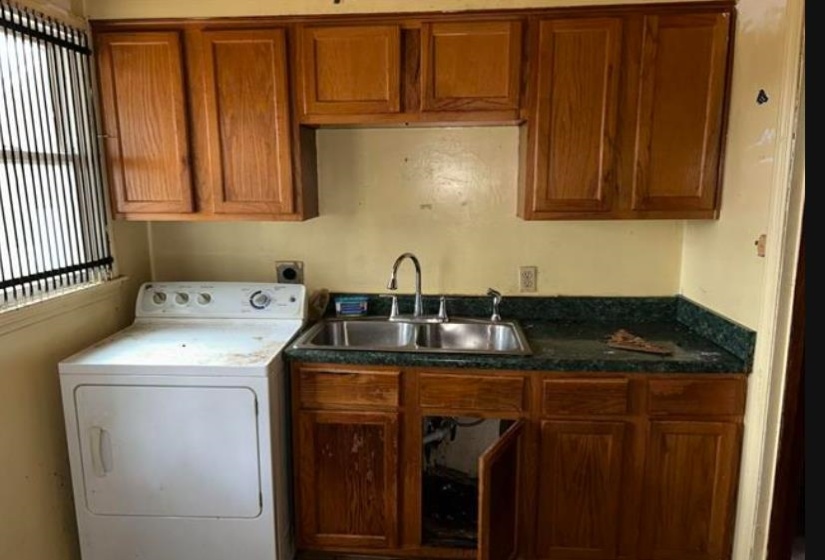Kitchen area featuring wood cabinetry, a double basin stainless steel sink, and a dark countertop