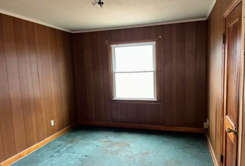 Room featuring vertical wood paneling, a single-pane window, and wall-to-wall carpeting