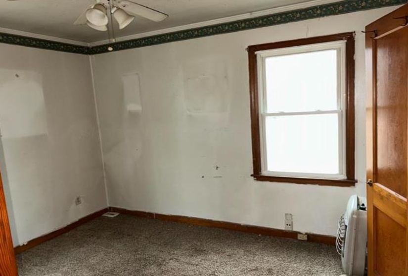 Carpeted room with a ceiling fan, a window with wood trim, wood baseboards, and a wood door