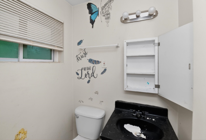 Bathroom featuring a window with blinds, a toilet, a wall-mounted medicine cabinet with shelving, a black vanity with an integrated sink, and a three-bulb light fixture