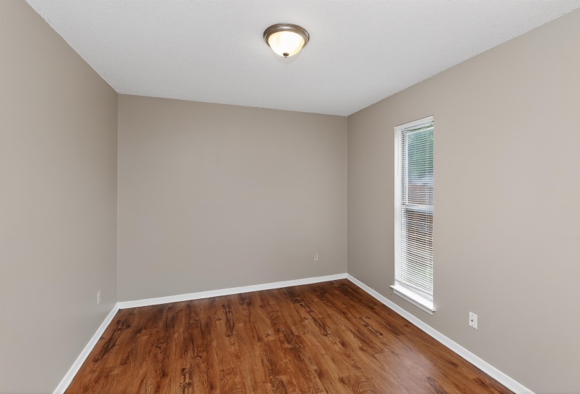 Neutral-toned room featuring rich wood-finish flooring, white baseboards, and a single window with blinds