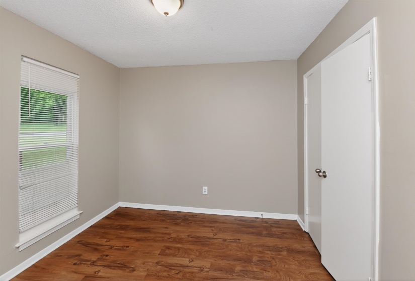 Interior space featuring wood-finish flooring, neutral wall paint, white baseboards, a single window with blinds, and a flush-mount ceiling light fixture