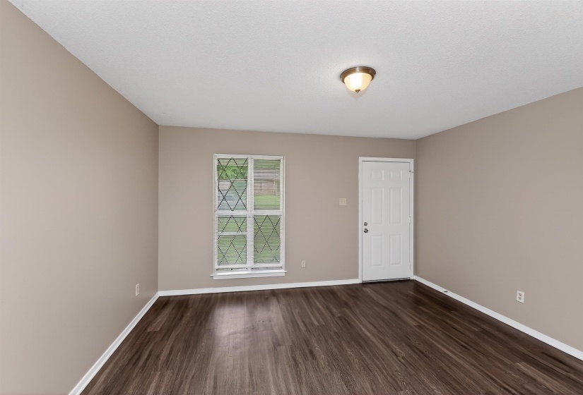 Interior room featuring wood-finish flooring, neutral wall tones, a white paneled door, a window with decorative muntins, and a ceiling-mounted light fixture