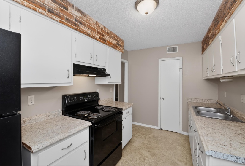 Bright kitchen featuring white cabinetry, a black electric range, a double basin stainless steel sink, and light-toned countertops