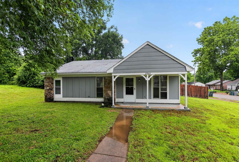 Ranch-style exterior featuring gray siding, stone accents, a covered front porch, a gabled roofline, and a concrete walkway
