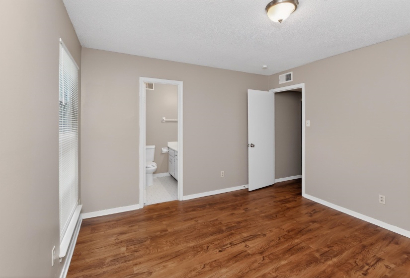 Spacious room featuring rich wood-finish flooring, neutral wall tones, and a window with blinds