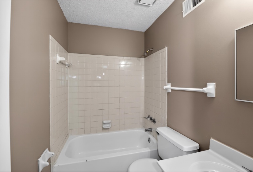 Bathroom featuring a white porcelain bathtub with tiled surround, a white toilet, and a white vanity with an integrated sink