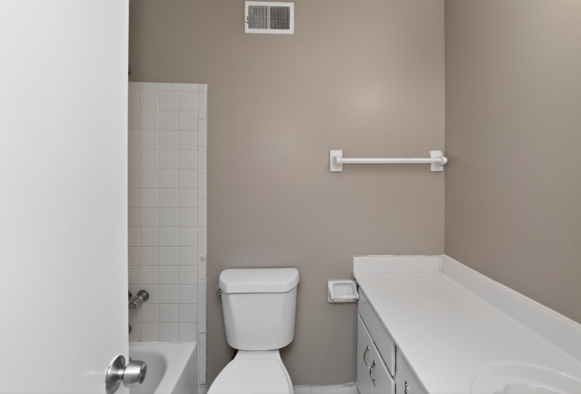 Bathroom featuring a white toilet, integrated vanity sink, and white tile tub surround