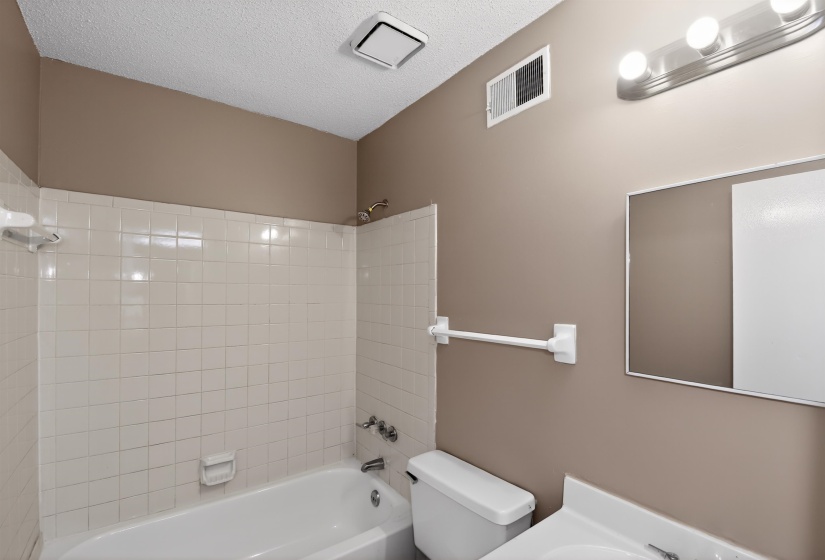 Bathroom featuring a white tub, white tiled surround, wall-mounted mirror, and vanity with an integrated sink