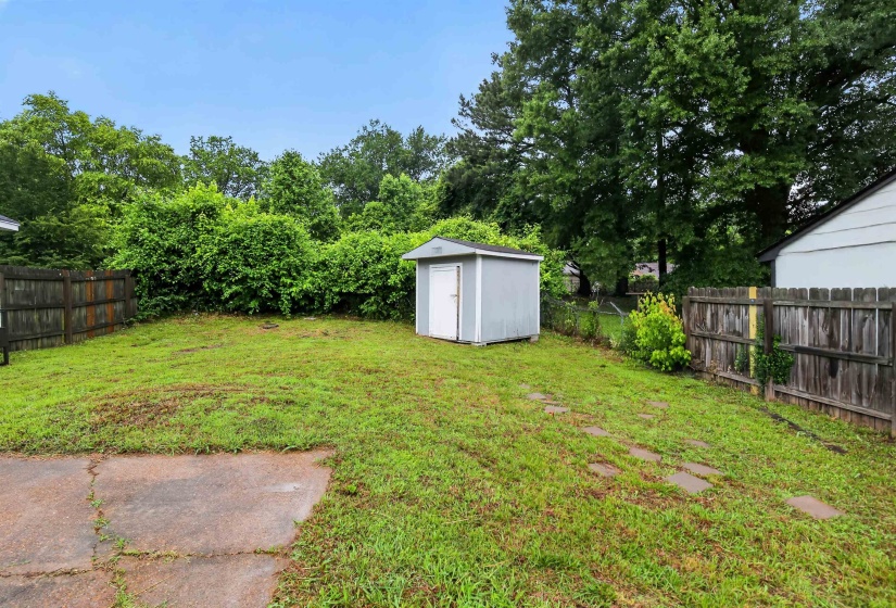 Expansive backyard featuring a gray storage shed, a concrete patio area, and mature perimeter trees
