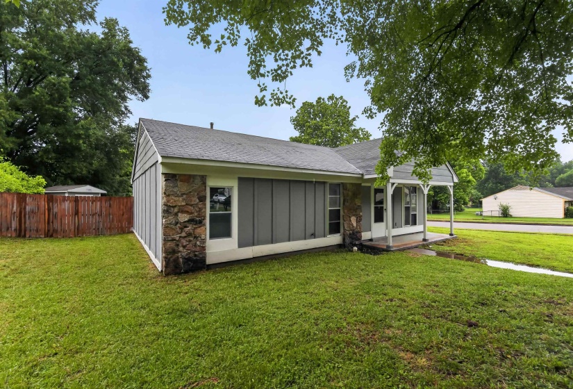 Exterior featuring gray vertical siding, natural stone accents, a covered front porch with white columns, a dark shingle roof, and a wood privacy fence