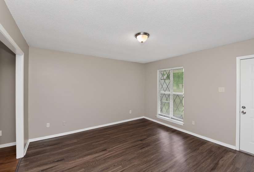 Interior space featuring wood-finish flooring, light taupe walls, white trim, and a window with decorative muntins