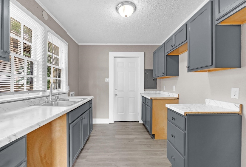 Kitchen featuring gray shaker-style cabinetry, white countertops with integrated backsplash, a double basin stainless steel sink, and wood-finish flooring