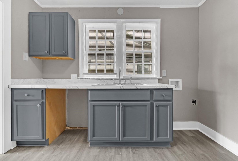 Kitchenette featuring gray cabinetry, a double basin stainless steel sink, wood-finish flooring, a white countertop, and a window with blinds