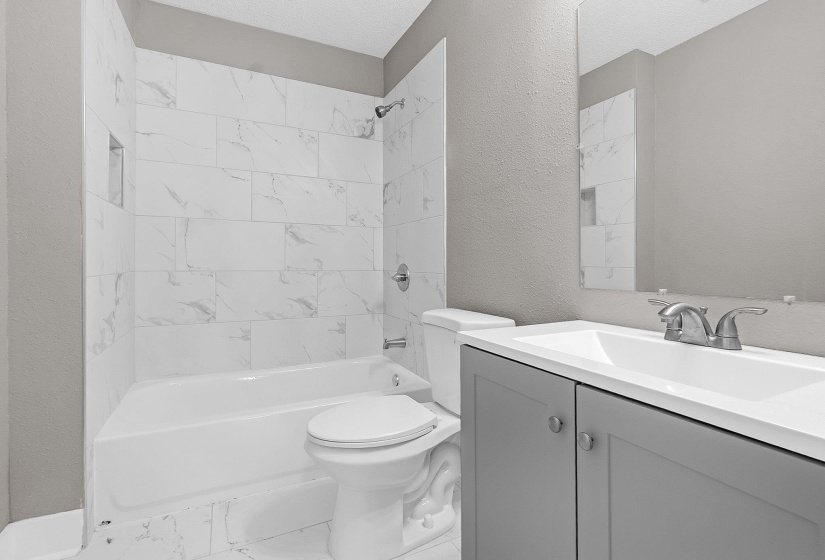 Bathroom featuring a white subway tile shower surround with a recessed niche, a white tub, a toilet, a gray vanity with a white integrated sink, and a wall-mounted mirror