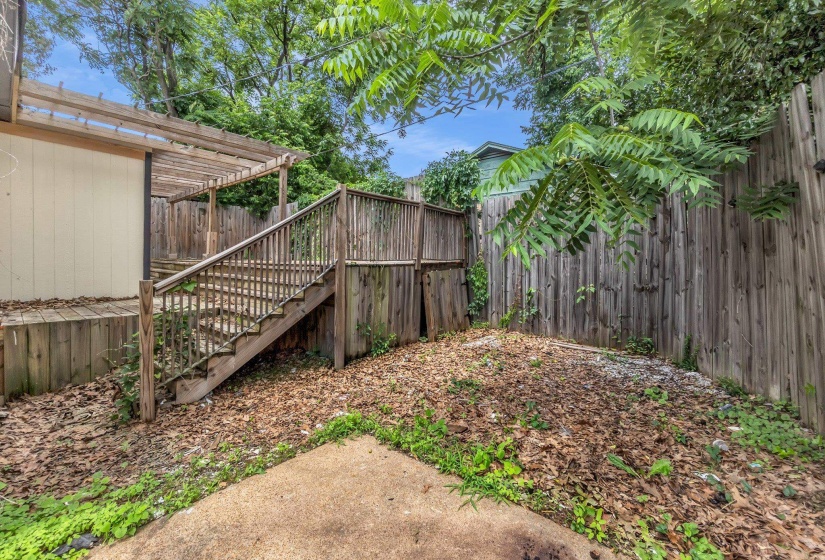 Wood deck with steps and a pergola, bordered by a privacy fence and mature trees