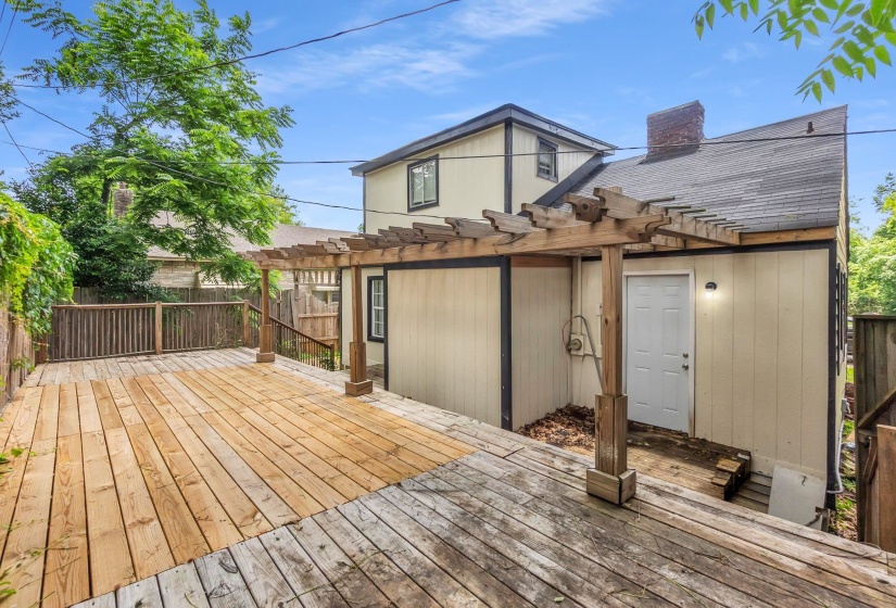 Spacious outdoor deck with a wooden pergola, bordered by a wooden fence