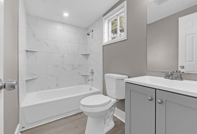 Full bathroom featuring a white tub with subway-style tiled surround, integrated shower, and recessed wall shelves