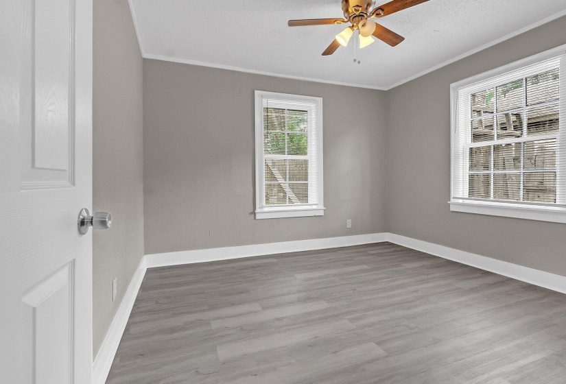 Room featuring light gray walls, wood-finish flooring, white trim, and two double-hung windows with blinds