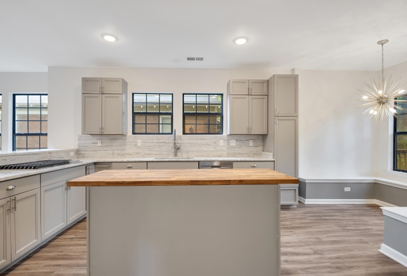 Kitchen featuring an expansive center island with a wood-finish countertop, light gray cabinetry, and a gas range