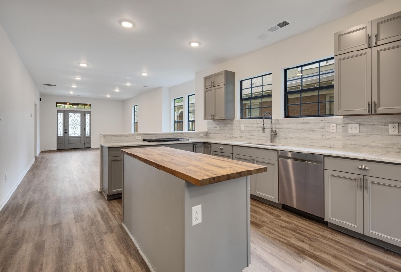Spacious kitchen featuring an island with butcher block countertop, grey cabinetry, stainless steel appliances, and light-toned countertops with a matching backsplash