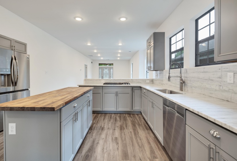 Contemporary kitchen featuring a large wood-top island, light gray cabinetry, stainless steel appliances, and wood-finish flooring