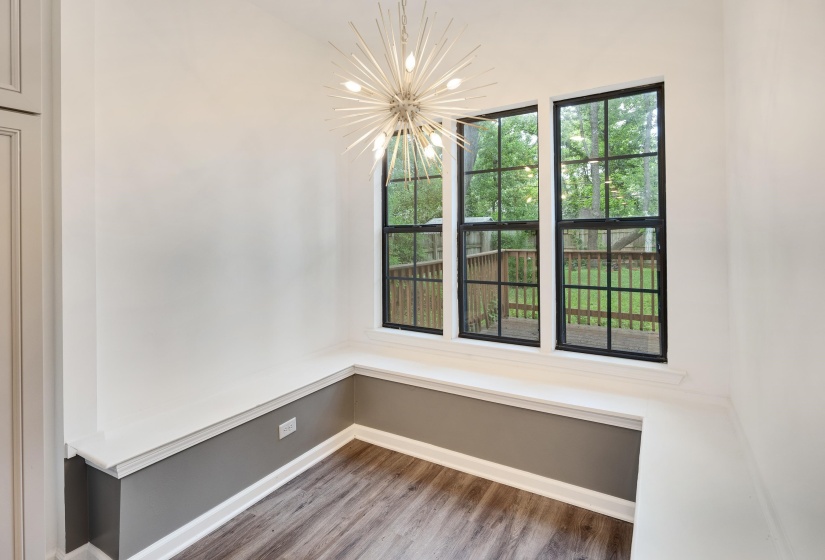 Corner nook featuring three expansive windows with black grids, a built-in bench, wood-finish flooring, a modern sputnik chandelier, and a two-tone wall treatment