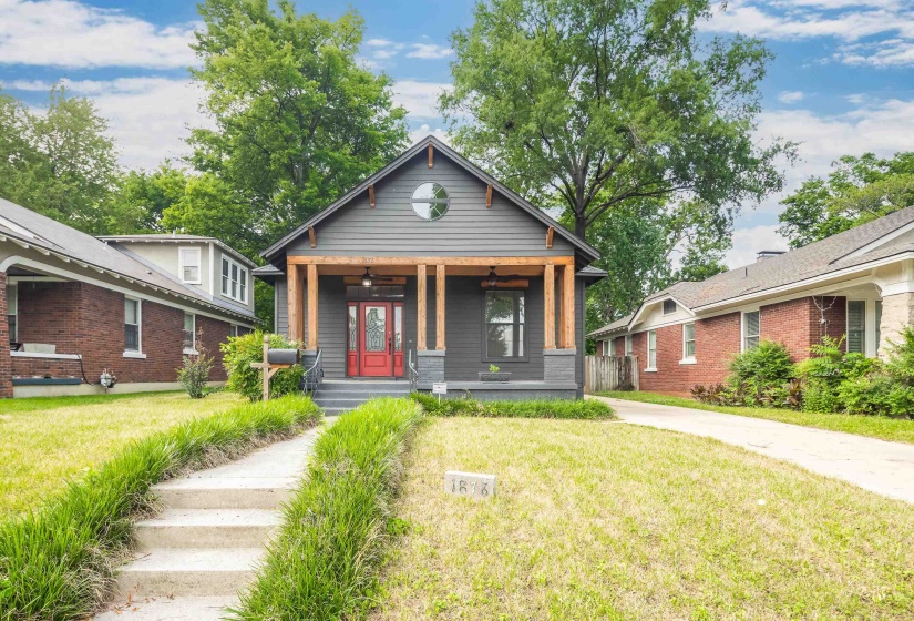 Contemporary Craftsman-style exterior featuring dark gray siding, a prominent red entry door, a covered porch with natural wood columns, a circular window on the upper gable, and a concrete walkway leading to the entrance